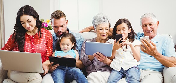Eine Großfamilie mit zwei Kindern sitzt auf einem Sofa und alle schauen auf einen Computer oder ein Tablet