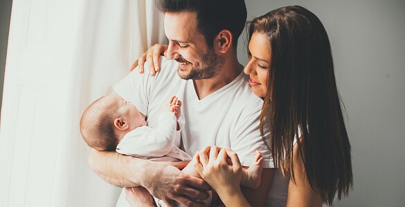 Ein Mann und eine Frau, die ein Baby im Arm des Mannes anlächeln