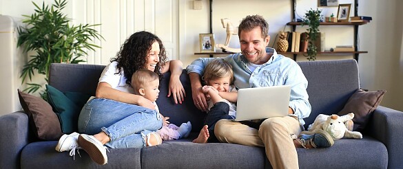 Eine vierköpfige Familie sitzt auf einem Sofa und schaut auf einen Computer
