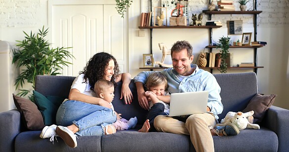 Eine Familie mit zwei Kindern, die auf einem Sofa sitzt und auf einen Computer schaut