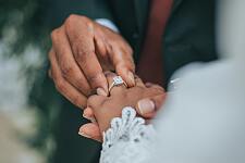 Eine männliche Hand steckt der Hand der Braut den Ehering auf