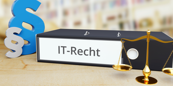 Ein Ordner leigt auf dem Tisch und ist beschriftet mit IT-Recht, daneben steht eine Waage und im Hintergrund sind zwei Paragraphenzeichen zu sehen