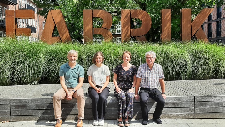 Die Personen des Referats 43 sitzen auf einer Mauer vor dem Schriftzug Fabrik
