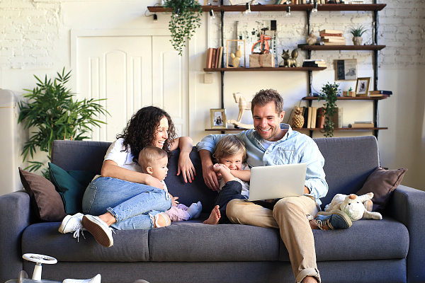Eine Familie mit zwei Kindern die auf einem Sofa sitzt und auf einen Computer schaut