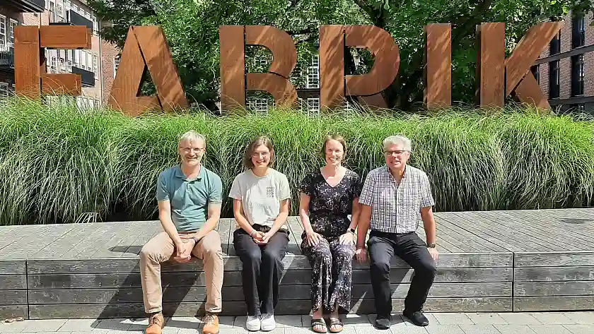 Die Personen des Referats 43 sitzen auf einer Mauer vor dem Schriftzug Fabrik