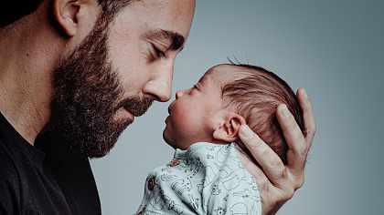 Ein Mann hält ein Baby in seiner linken Hand und schaut es an.