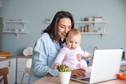 Eine Frau hält ein Baby und arbeitet am Computer
